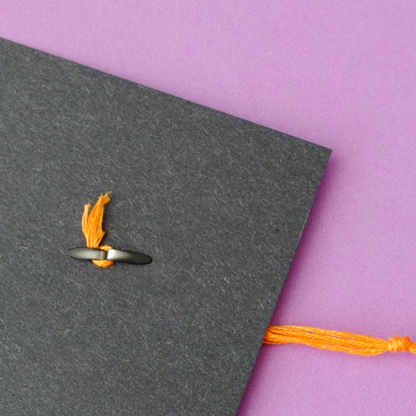 This photo illustrates how to attach the tassle to the mortar board cap using a black fastener.