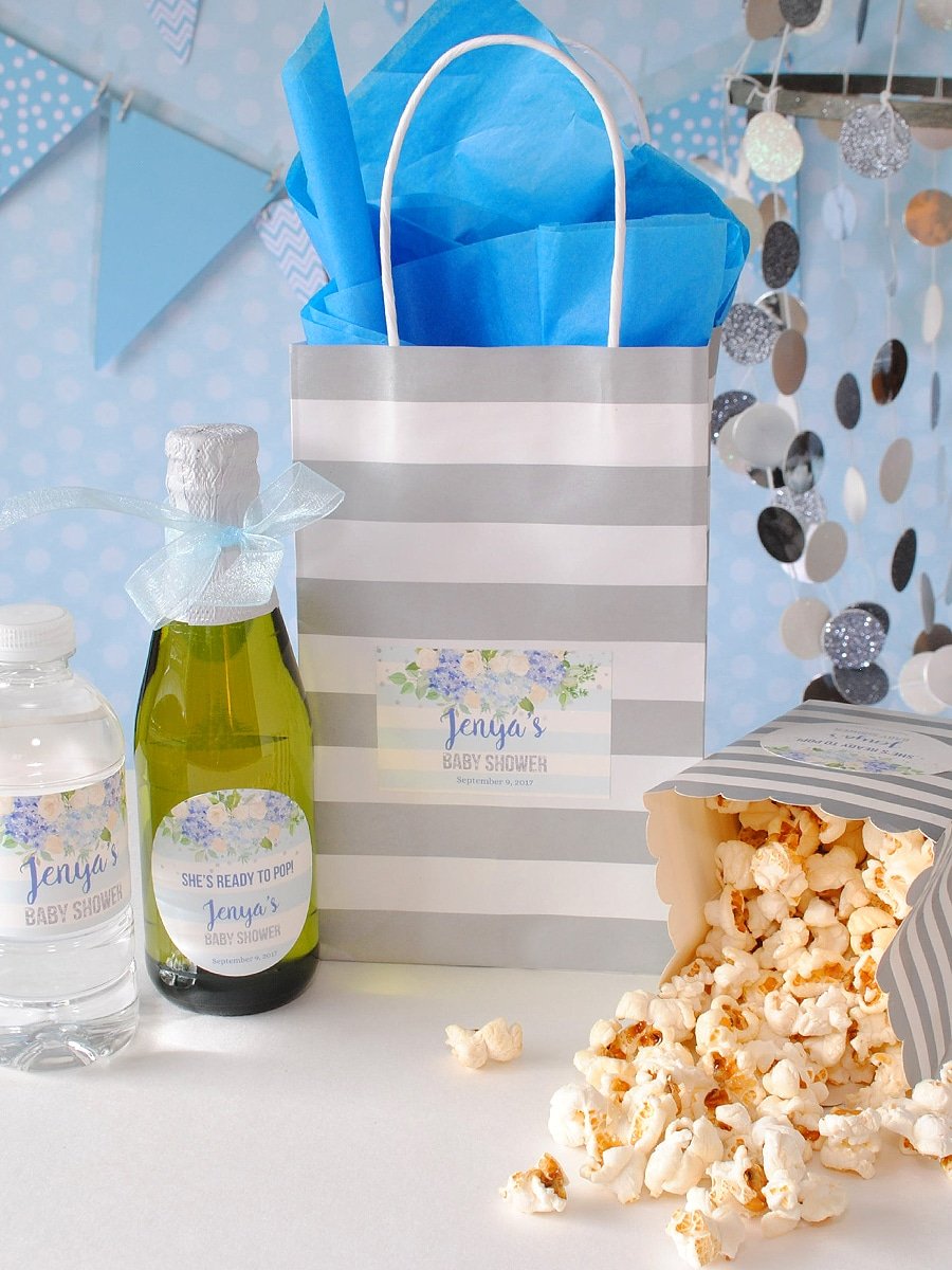 Create a goody bag for a baby boy shower and include edible items with personalized labels. Mini sparkling cider, mini bottled water, and kettle corn. All labeled with a "She's Ready to Pop" personalized sticker.