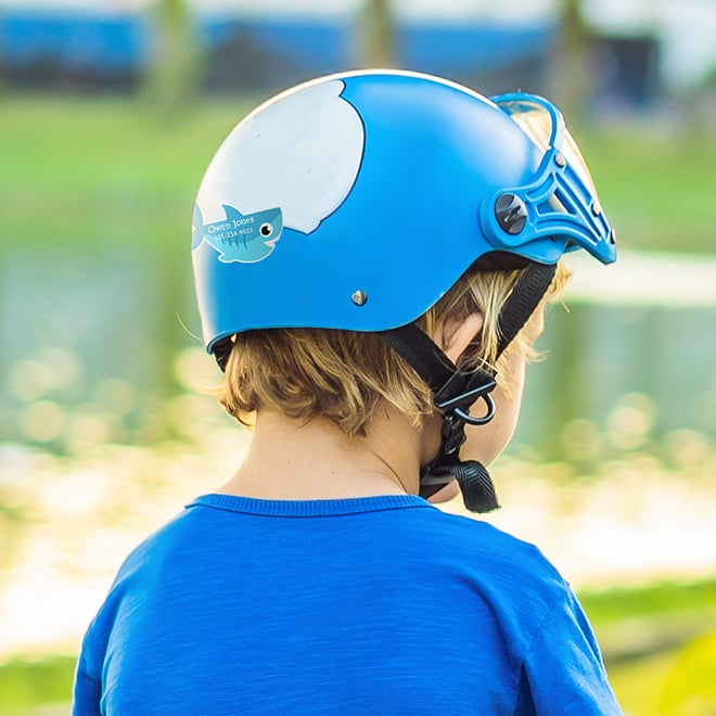 Child wearing a helmet with a shark shaped name label. Make your own shark labels with your child's name. Name labels for kids safety helmets for bike riding, skate boarding and more.
